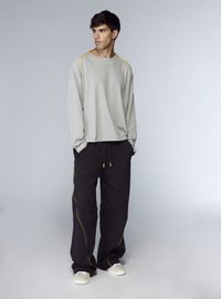 Camicia grigio chiaro a maniche lunghe con cuciture laterali gialle, abbinata a pantaloni cargo neri con dettagli gialli e vita elasticizzata. Scarpe bianche.