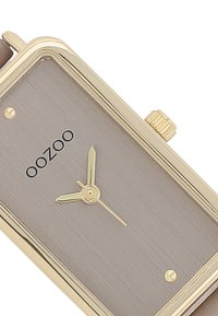 Montre rectangulaire dorée avec un cadran gris brossé, des aiguilles minimalistes et une couronne dorée. Équipée d'un bracelet en cuir pour un look classique.