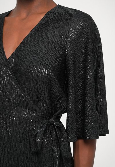 Robe noire enveloppante en tissu texturé avec un subtil scintillement. Décolleté en V et larges manches volantées. Détail de taille nouée.