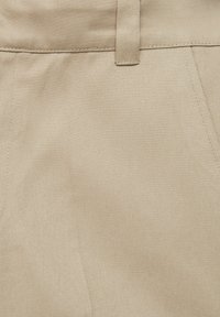 Gros plan d'un tissu beige montrant la ceinture, la passant de ceinture et la couture de la couture latérale sur un pantalon.