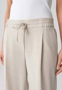 Lichtbeige, relaxed-fit broeken met een elastische tailleband, koordsluiting en zijzakken; textiel met een subtiele structuur en plooien.