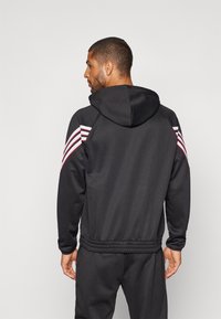 Black athletic hoodie with a hood, smooth texture, featuring red and white striped accents on the shoulders, and elasticated hem and cuffs.