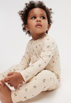 Pyjama en coton beige à manches longues et jambes longues, présentant un motif floral de petites fleurs roses et de feuilles vertes. Fermeture à boutons devant.