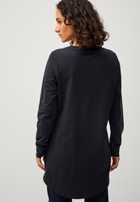 Zwarte langemouwshirt met een ronde halslijn, gemaakt van zachte stof. Heeft een rechte snit en een langere achterzoom voor extra bedekking.