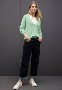 Cardigan vert menthe, moelleux, avec un col en V et des boutons, associé à un pantalon large en denim foncé et des baskets blanches. Textures lisses et style décontracté.