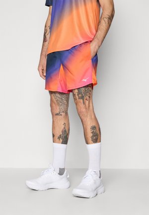 Ensemble de vêtements de sport avec un haut dégradé orange et bleu et un short assorti. Comprend des chaussures et des chaussettes blanches, avec des tatouages visibles sur les jambes.