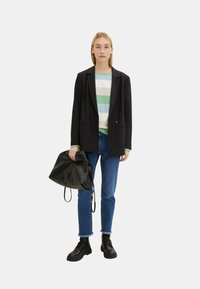 Schwarze, doppelt geknöpfte Blazer über einem gestreiften Pulli in Grün, Blau und Weiß. Blaue Jeans mit ausgefransten Säumen und schwarzen Schnürstiefeln. Schwarze Tasche.