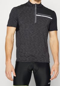 Camiseta atlética negra de manga corta con cuello con cremallera, tejido texturizado, franja de acento blanca y patrón de puntos en el pecho; acompañada de pantalones cortos negros.