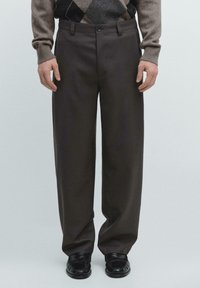 Braune, maßgeschneiderte Hose mit geradem Schnitt, mit flacher Vorderseite, Seitentaschen und glatter Textur, kombiniert mit schwarzen Loafers.