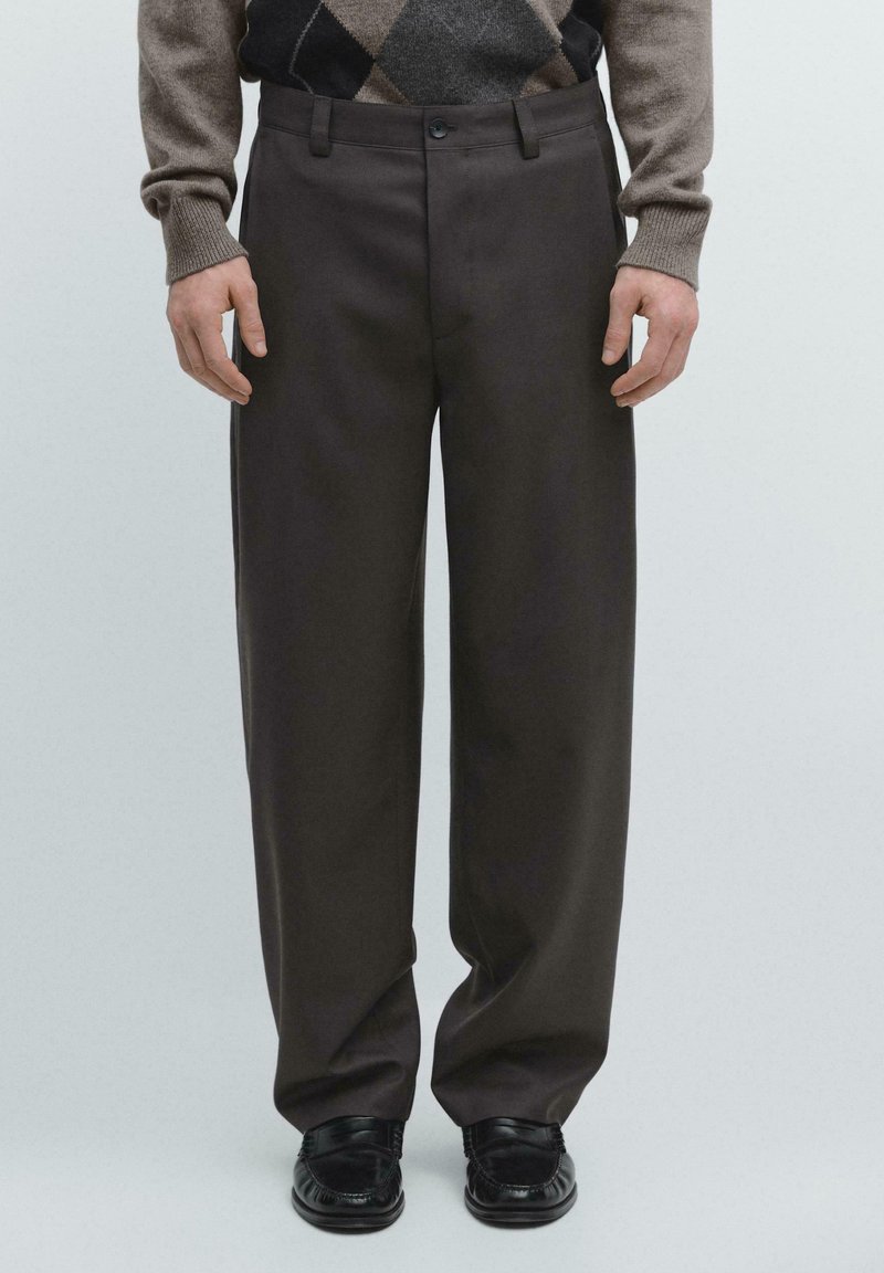 Braune, maßgeschneiderte Hose mit geradem Schnitt, mit flacher Vorderseite, Seitentaschen und glatter Textur, kombiniert mit schwarzen Loafers.