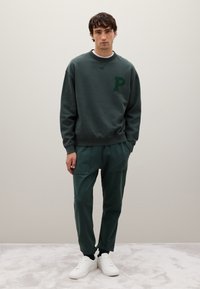 Donkergroen sweatshirt met een geborduurd "P" logo, gecombineerd met bijpassende tapered sweatpants en witte sneakers, met twee voorzakken.
