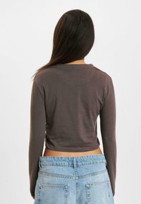 Brown long-sleeve crop top with a round neckline and smooth texture, paired with high-waisted light blue denim shorts.