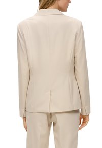 Beige op maat gemaakte blazer met een notch revers, gestructureerde schouders en een gladde textuur. Voorzien van een rugventilatie en schuine mouwnaden.
