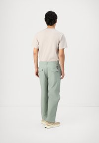 Lichtbeige t-shirt gecombineerd met lichtgroene broek, met een relaxte pasvorm, achterzakken en een klein logo-etiket op de tailleband.
