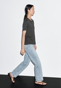 Gray short-sleeved t-shirt, light blue straight-leg jeans, and brown sandals. Model walking against a white backdrop.