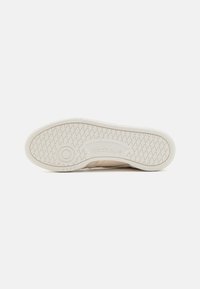 Outsola tenisky Reebok v off-white farbe, s textúrovaným gripovým vzorom a kruhovým logom. Hladký povrch s jemnými detailovými akcentmi.