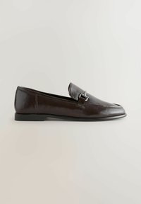Mocassin en cuir marron foncé avec détail de boucle métallique argentée, talon bas et finition lisse, montré en profil sur un fond uni.