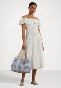 Bela off-the-shoulder obleka z volančki na vrhu in eyelet detajli; modra prugačka torbica z zlatim okovjem in ravni espadril čevlji.