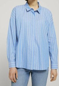 Ljusblå skjorta med knappar, vita vertikala ränder, långa ärmar, en spetsig krage och en avslappnad passform, med knappslutning vid ärmsluten.