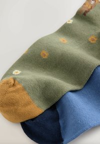 Ponožky s potlačou s zeleným základom a žltými a bielymi kvetinovými vzormi, béžovou špičkou a modrou časťou na päte. Mäkká pletená textúra.