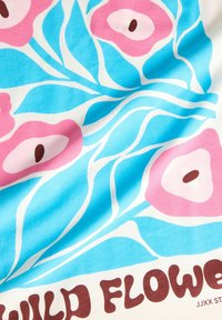 Tissu avec un motif floral coloré comprenant des fleurs roses, des feuilles bleues et un fond blanc, avec le texte "WILD FLOWER" en lettres marron.