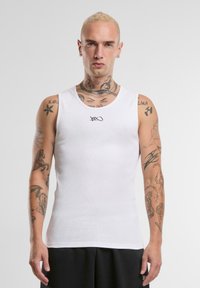 Hvit ermeløs tanktop med en tettsittende design, med en liten svart logo ved halsen. Slett tekstur, ingen mønstre eller aksenter.