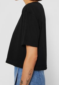 Svart kortärmad t-shirt i bomull, med korta ärmar och rund halsringning. Enkel design med en slät yta.