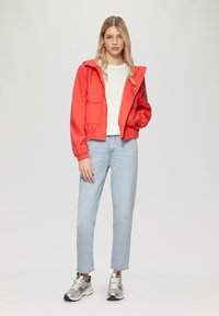 Rode, met een capuchon jack met twee voorzakken, gecombineerd met een witte top en lichtblauwe jeans. Model draagt zilveren sneakers.