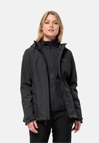 Giacca nera impermeabile con zip frontale, cappuccio e polsini regolabili, indossata sopra un top in fleece nero. Texture liscia, design compatto.