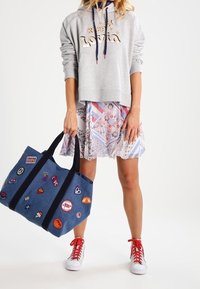 Sudadera gris recortada con el texto "Keep Loving", falda floral y de rayas, bolsa de mano de mezclilla azul con parches y zapatillas rojas.