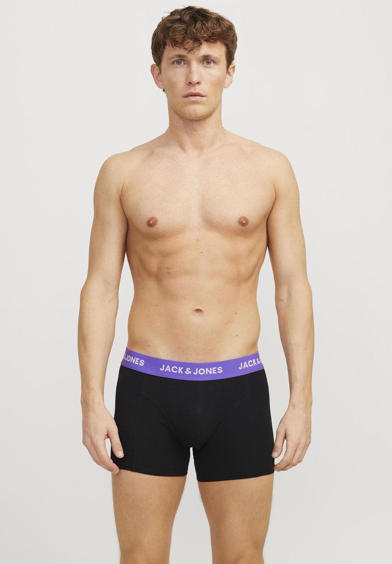 Schwarze Boxer-Shorts mit einem lila elastischen Bund, der das Logo "JACK & JONES" trägt. Der Stoff scheint glatt und eng anliegend zu sein. Das Modell ist oberkörperfrei.