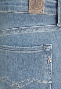 Jeans in denim azzurro chiaro con tasca posteriore decorata da cuciture a motivo, piccolo emblema metallico "R" e patch in pelle sopra la cintura.