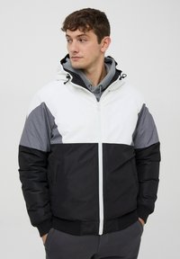 Giacca imbottita con chiusura a zip, cappuccio e design a blocchi di colore in bianco, grigio e nero con accenti in tessuto testurizzato.