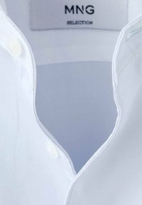 Chemise à col blanc avec un design à boutons, texture de tissu lisse et détails de couture subtils. Étiquette de marque visible à l'intérieur du col.