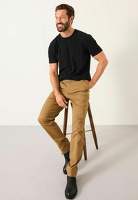 Schwarzes Kurzarm-T-Shirt kombiniert mit hellbraunen geraden Hosen und schwarzen Knöchelstiefeln. Das Outfit zeichnet sich durch ein minimalistisches Design und eine glatte Textur aus.