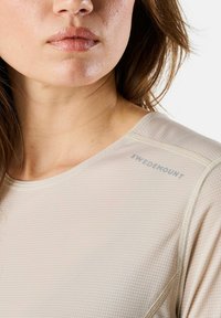 Lichtbeige sporttop met korte mouwen, gestructureerde stof en een ronde halslijn. Bevat subtiele "Swedemount" branding op de schouder.