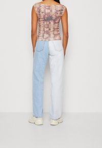 Fitovaný hnědý vzorovaný top s krátkým rukávem, spárovaný s světle modrými dvoubarevnými širokými džíny a béžovými teniskami. Pozadí je čistě bílé.