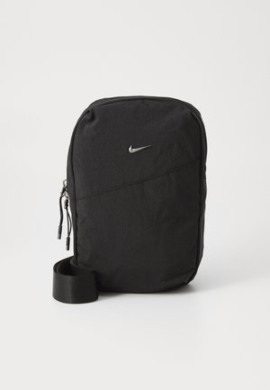 Sac à dos noir Nike avec un tissu texturé, un design élégant, un logo argenté prominent et une sangle noire enroulée à la base. Ouverture zippée.