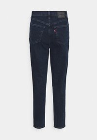 Jean slim bleu foncé avec poches arrière, étiquette rouge Levi's sur la poche droite et écusson en cuir de la marque sur la ceinture.