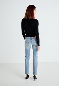 Black cable-knit sweater, light blue fitted jeans with a leather patch, and black high-heeled shoes, viewed from the back.