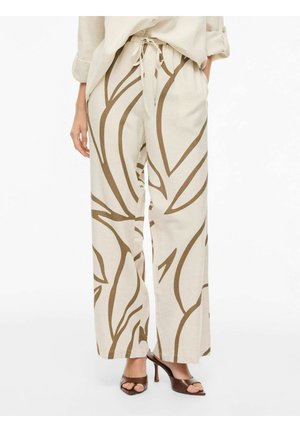 Beige bukser med vide ben og abstrakte brune bladmønstre, kombineret med brune åbne hæle med hæl, modelens hånd i lommen.