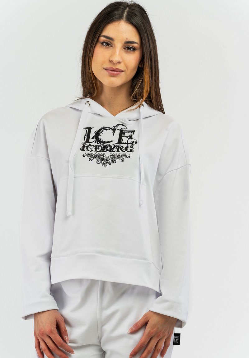 Sudadera blanca con capucha y logo frontal en negro, con un corte holgado, mangas largas y detalles de cordón. Textura suave.
