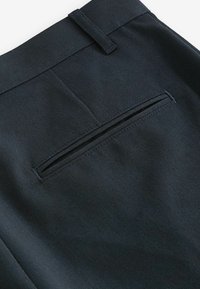 Schwarze Hose aus glattem, strukturiertem Stoff. Eine Gesäßtasche ist sichtbar, mit einem dezenten Reißverschluss, der in das Design integriert ist.