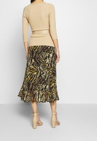 Beige ribbad topp med trekvartsärmar, i kombination med en flytande svart kjol med ett gult och brunt abstrakt mönster samt en vågig nederkant.