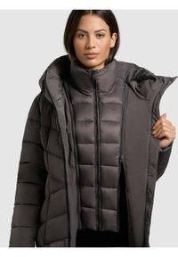 Chaqueta acolchada de color gris oscuro, aislante, con un alto cuello y cremalleras dobles, que presenta un diseño acolchado y una textura suave.