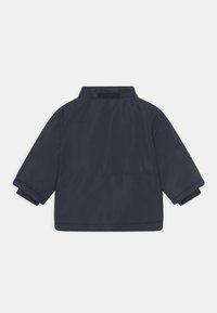 Giacca blu navy con colletto classico, maniche lunghe e chiusura in velcro. Tessuto liscio con design leggero, con polsini arrotolati.