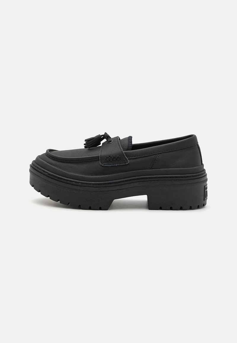 Mocassin en cuir noir avec semelle plateforme épaisse et détail pompon sur le dessus, présenté en profil latéral sur fond blanc.