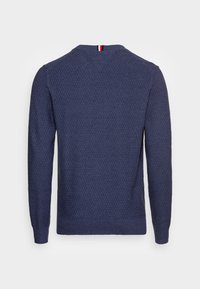 Granatowy sweter o fakturze z dekoltem w łódkę, długimi rękawami i kontrastującym paskiem w kolorach czerwonym, białym i niebieskim z tyłu przy linii szyi.