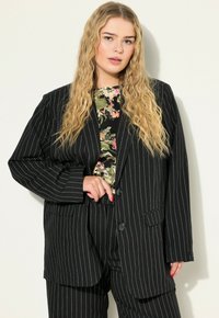 Černý blazer s pruhy a volným střihem, s jedním knoflíkem a dvěma předními kapsami, nošený přes top s květinovým vzorem.