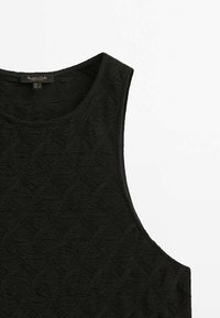 Top noir sans manches avec motif texturé en forme de losanges et vagues, col rond et étiquette de marque près du col.